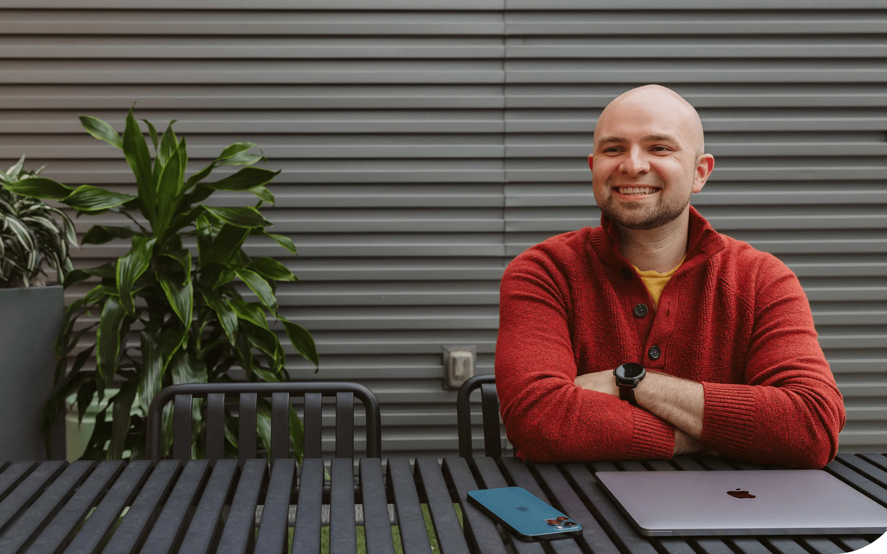 Person sitting outside, smiling with a closed laptop in front them on a table