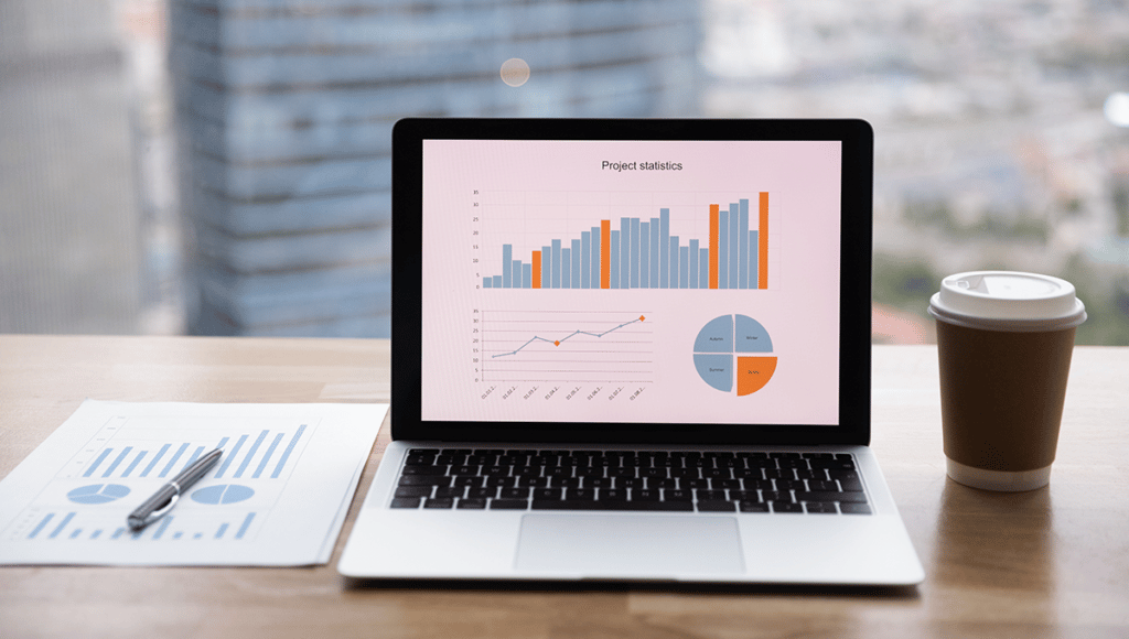 laptop with graphs next to a coffee cup and printed graphs on a table